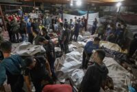 Foto konferensi pers yang beredar memperlihatkan para anggota staf medis berdiri di antara jasad-jasad yang ditutupi. (Foto Istimewa)