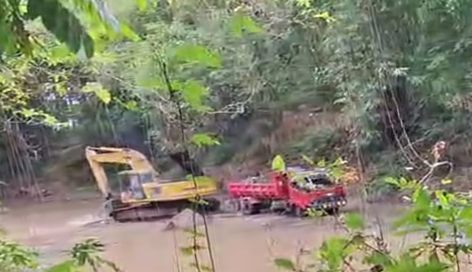 Excavator terlihat sibuk menggali dan mengangkut material ke dalam dump truck di lokasi tambang ilegal Bone