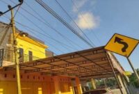 Tiang listrik miring berdiri tepat di sisi jalan, dengan kabel-kabel listrik terbentang sangat dekat dengan atap rumah warga Bulolohe, Bulukumba.