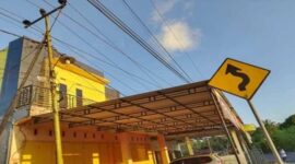 Tiang listrik miring berdiri tepat di sisi jalan, dengan kabel-kabel listrik terbentang sangat dekat dengan atap rumah warga Bulolohe, Bulukumba.