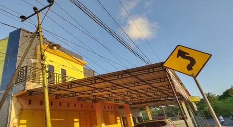 Tiang listrik miring berdiri tepat di sisi jalan, dengan kabel-kabel listrik terbentang sangat dekat dengan atap rumah warga Bulolohe, Bulukumba.