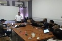 Dewan Pendiri Serikat Insan Media (SIM), Ibhe Ananda (berdiri mengenakan kemeja putih), memimpin rapat bersama anggota SIM di sebuah ruang pertemuan.