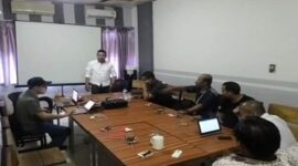 Dewan Pendiri Serikat Insan Media (SIM), Ibhe Ananda (berdiri mengenakan kemeja putih), memimpin rapat bersama anggota SIM di sebuah ruang pertemuan.