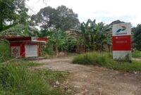 Bangunan Pertashop tampak terbengkalai dan tidak terawat, dengan cat yang memudar dan rumput liar yang merajalela.