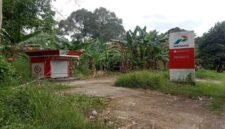 Bangunan Pertashop tampak terbengkalai dan tidak terawat, dengan cat yang memudar dan rumput liar yang merajalela.