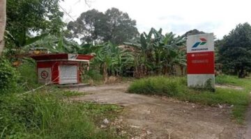 Bangunan Pertashop tampak terbengkalai dan tidak terawat, dengan cat yang memudar dan rumput liar yang merajalela.