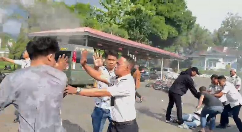 Sejumlah pria berpakaian sipil bersama oknum petugas berseragam putih terlibat aksi saling tarik saat berupaya mengamankan seorang mahasiswa di tanah. Insiden mencekam ini terjadi di tengah aksi unjuk rasa AMPH terkait darurat narkoba yang berakhir chaos.