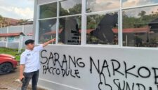Petugas Lapas menunjuk kaca bangunan yang pecah serta coretan pilox di dinding pasca-aksi demonstrasi AMPH, Senin (25/5/2026). Coretan bertuliskan 