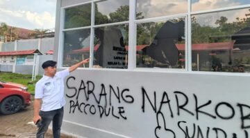 Petugas Lapas menunjuk kaca bangunan yang pecah serta coretan pilox di dinding pasca-aksi demonstrasi AMPH, Senin (25/5/2026). Coretan bertuliskan 