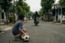 Ilustrasi bocah yang kakinya tertabrak sepeda motor dan penabrak langsung meninggalkan bocah tersebut setelah bermain bola di lapangan (Visual AI)