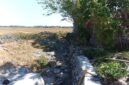 Kondisi proyek rehabilitasi jaringan irigasi Daerah Irigasi (DI) Pamukkulu di Kabupaten Takalar yang mangkrak dan belum rampung, memperlihatkan material batu serta struktur saluran yang terbengkalai di area persawahan.