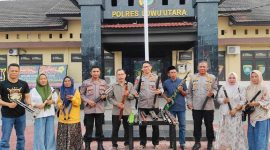 Warga dan aparat berfoto bersama menampilkan 60 senjata yang diserahkan secara sukarela di halaman Polres Lutra, bukti komitmen perdamaian Desa Munte dan Karondang.