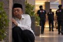 Ilustrasi dramatis Nusron Wahid yang digambarkan duduk bersembunyi di balik tembok sambil mengawasi situasi di sekitarnya. (Visual AI).